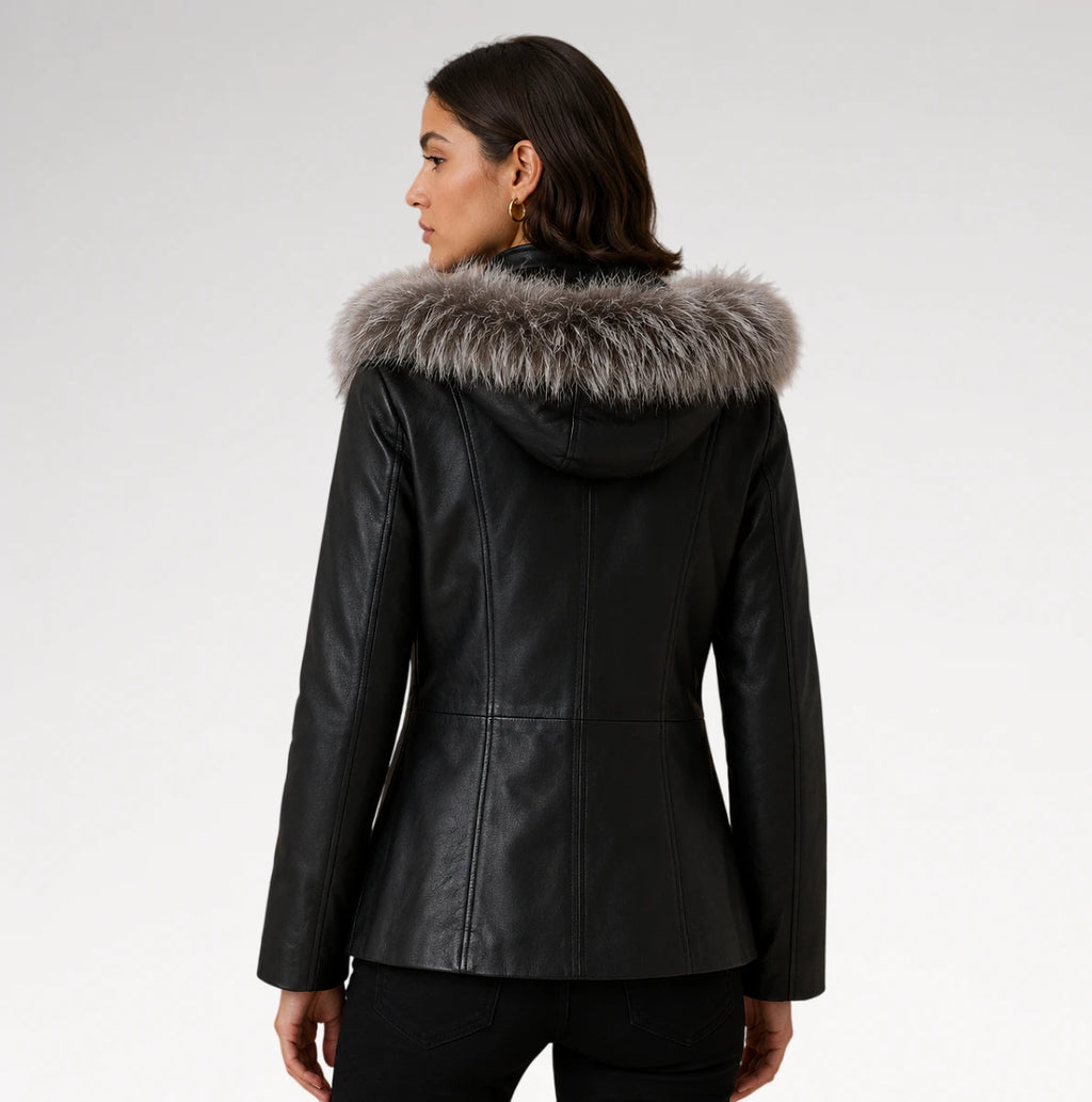 A woman shown from the back wearing a black faux-leather hooded jacket with a large gray and white faux-fur trim around the hood, against a light gray studio background.