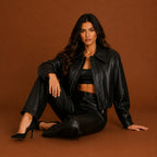 Woman wearing a black leather jacket and pants sitting on a brown background