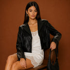 Woman wearing a black leather jacket over a white dress against a brown background