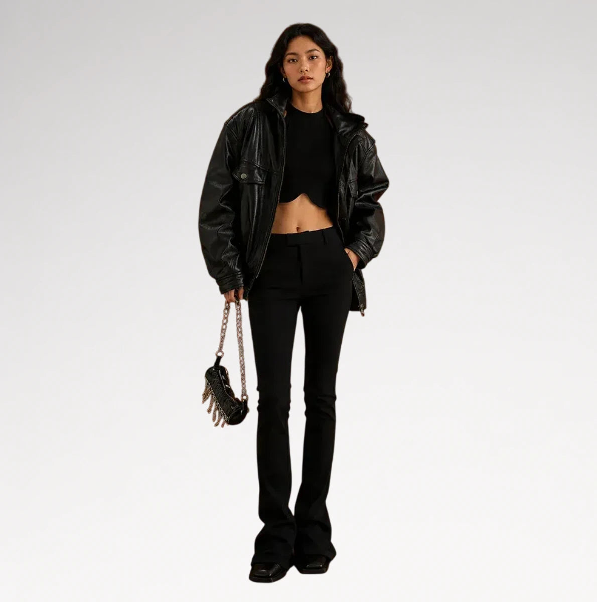 A model stands against a light gray studio background wearing a black faux-leather jacket, black crop top, black flared pants, and holding a small black handbag with a chain strap. Main image