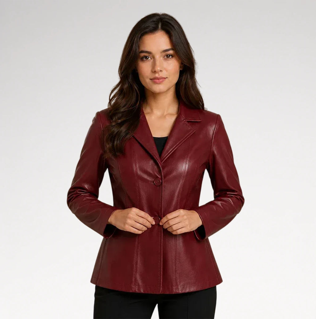 A woman modeling a fitted, long-sleeve blazer in a deep burgundy faux leather or leather-like material, styled over a black top and black pants against a light gray studio background.