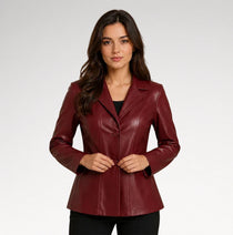 A woman modeling a fitted, long-sleeve blazer in a deep burgundy faux leather or leather-like material, styled over a black top and black pants against a light gray studio background.