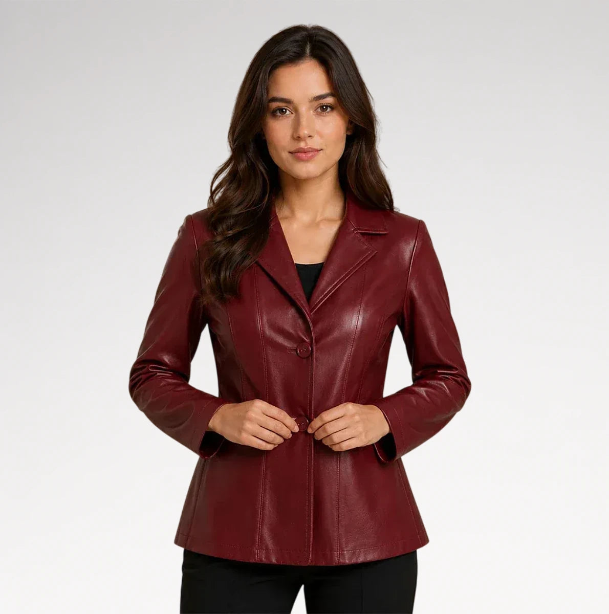A woman modeling a fitted, long-sleeve blazer in a deep burgundy faux leather or leather-like material, styled over a black top and black pants against a light gray studio background.