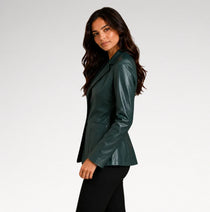 A woman wearing a dark green faux-leather blazer with black pants, photographed from the side against a light gray studio background.