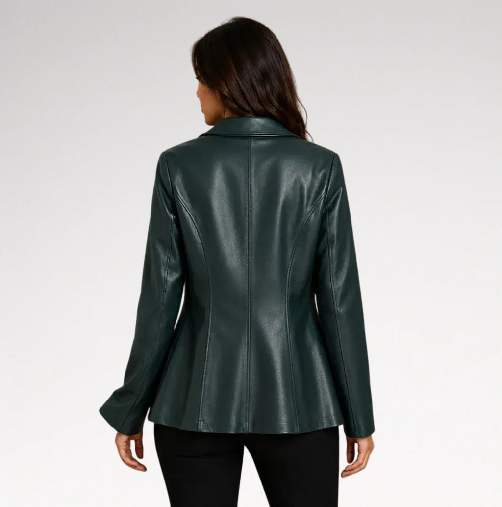 A woman viewed from the back wearing a dark forest green faux leather blazer with long sleeves and a structured collar, paired with black pants, against a light gray studio background.