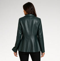 A woman viewed from the back wearing a dark forest green faux leather blazer with long sleeves and a structured collar, paired with black pants, against a light gray studio background.