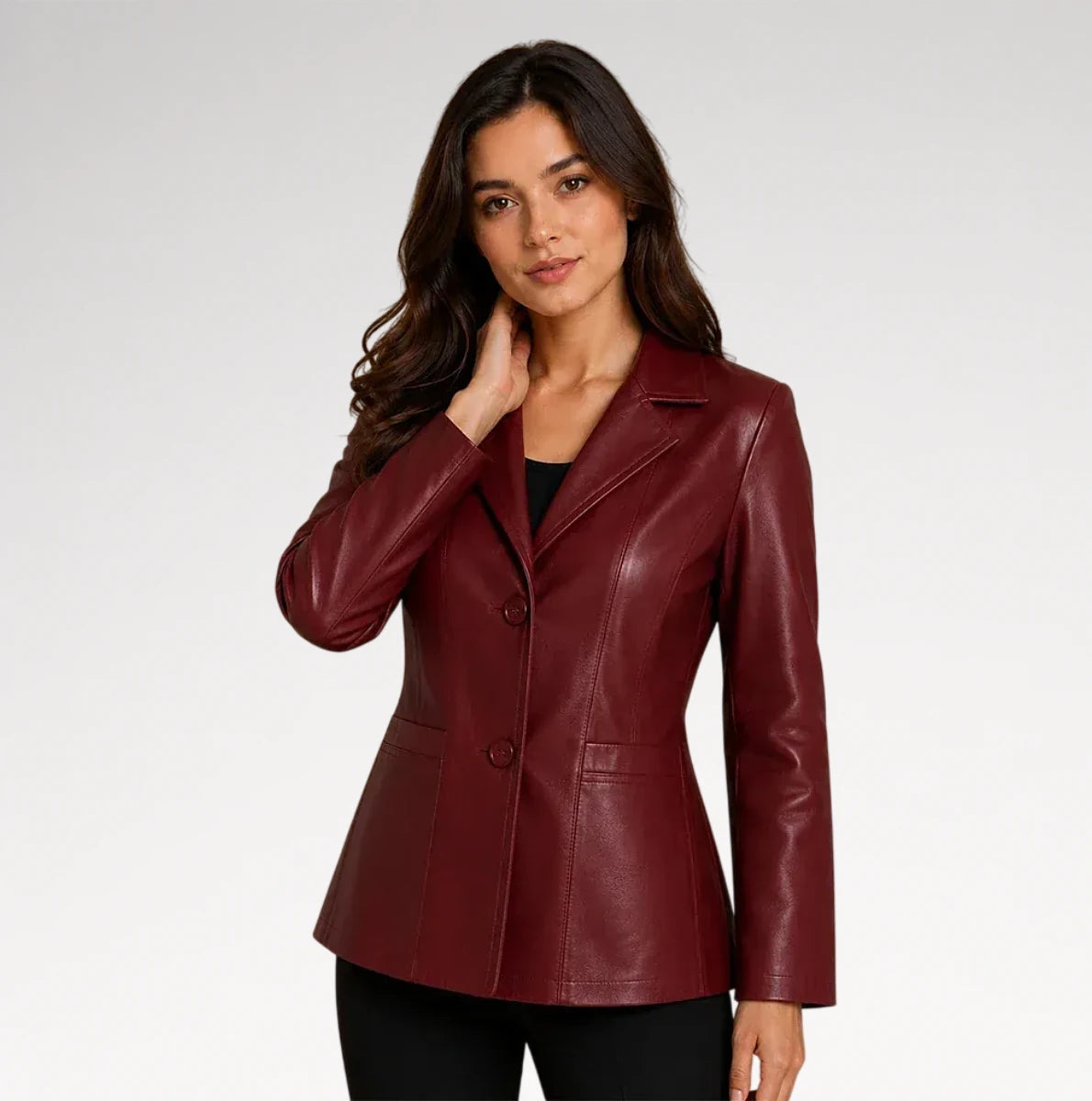 A woman modeling a fitted, dark burgundy faux-leather blazer with notch lapels and a two-button front, paired with black pants against a light gray studio background.