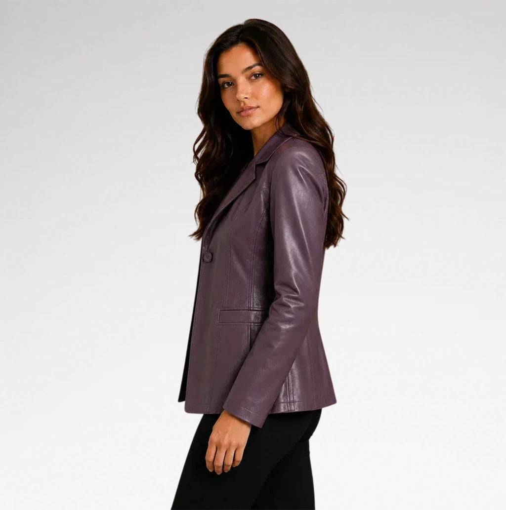 A woman wearing a fitted, glossy plum-purple leather blazer and black pants, photographed in profile against a clean light gray studio background.
