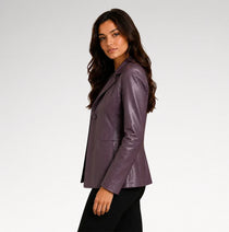 A woman wearing a fitted, glossy plum-purple leather blazer and black pants, photographed in profile against a clean light gray studio background.