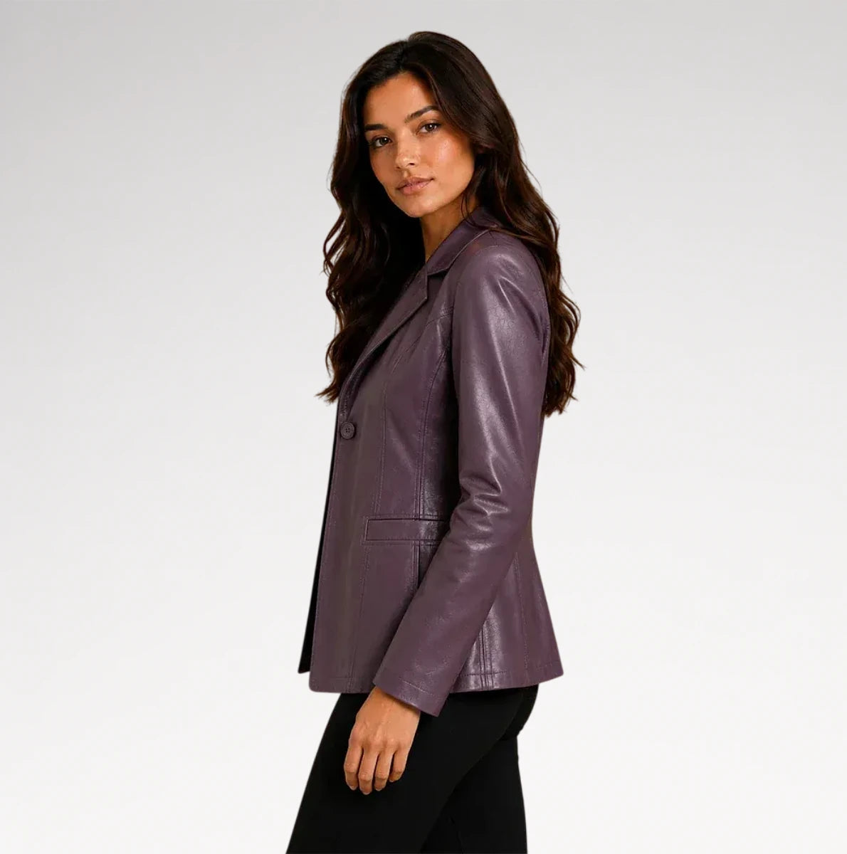 A woman wearing a fitted, glossy plum-purple leather blazer and black pants, photographed in profile against a clean light gray studio background.