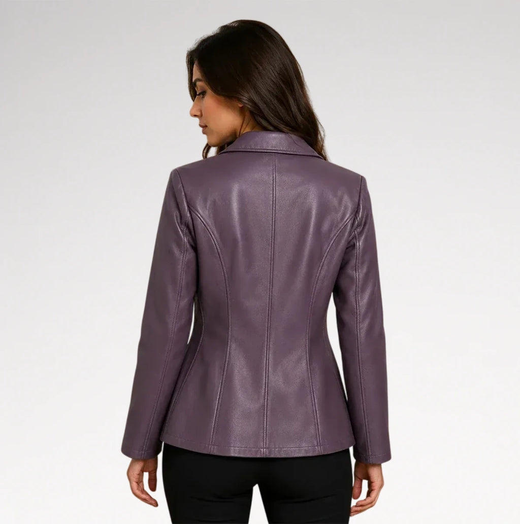 A woman shown from the back wearing a fitted, long-sleeve faux leather blazer in a muted plum purple color, paired with black pants, against a light gray studio background.