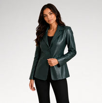 A woman modeling a dark green faux-leather blazer over a black top and black pants, photographed against a light gray studio background.