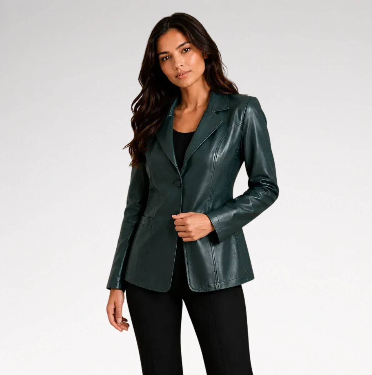 A woman modeling a dark green faux-leather blazer over a black top and black pants, photographed against a light gray studio background.