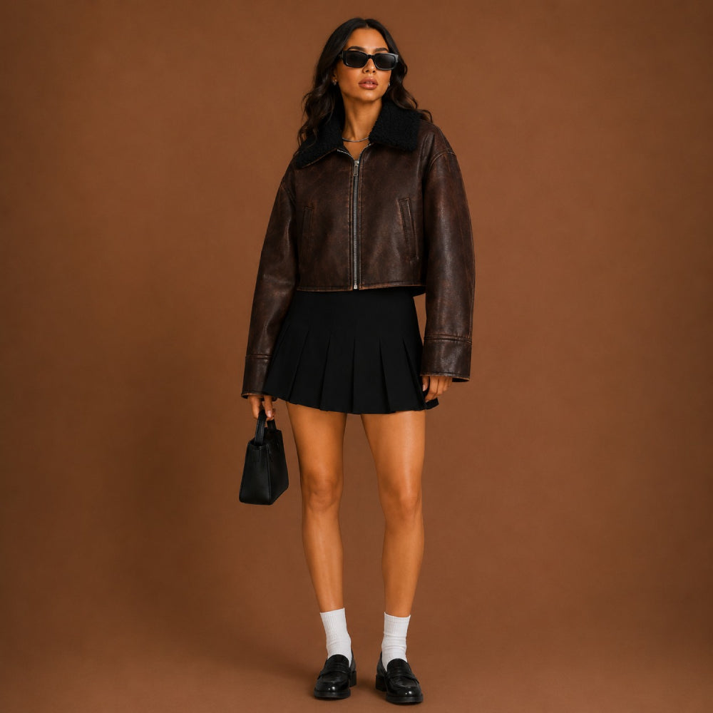 Woman wearing a brown leather jacket and black skirt against a brown background