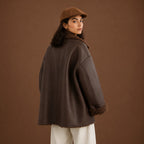 Person wearing a brown coat with fur trim against a brown background