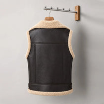 Black leather vest with beige fur lining on a hanger against a gray background