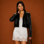 Woman wearing a black leather jacket over a white lace dress on a brown background