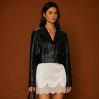 Woman wearing a black leather jacket and white lace skirt against a brown background