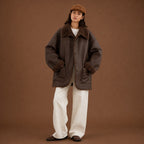Person wearing a brown coat with fur trim and white pants on a brown background