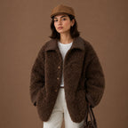 Woman wearing a brown teddy coat and cap against a brown background
