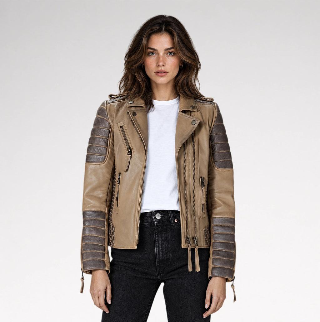 A woman modeling a tan faux-leather moto jacket with dark brown ribbed sleeve panels, a white t-shirt, and black jeans against a light gray studio background.