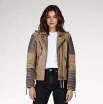 A woman modeling a tan faux-leather moto jacket with dark brown ribbed sleeve panels, a white t-shirt, and black jeans against a light gray studio background.