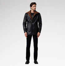 A man modeling a black leather jacket with a brown suede-like hood, paired with black jeans and black boots, against a light gray studio background.