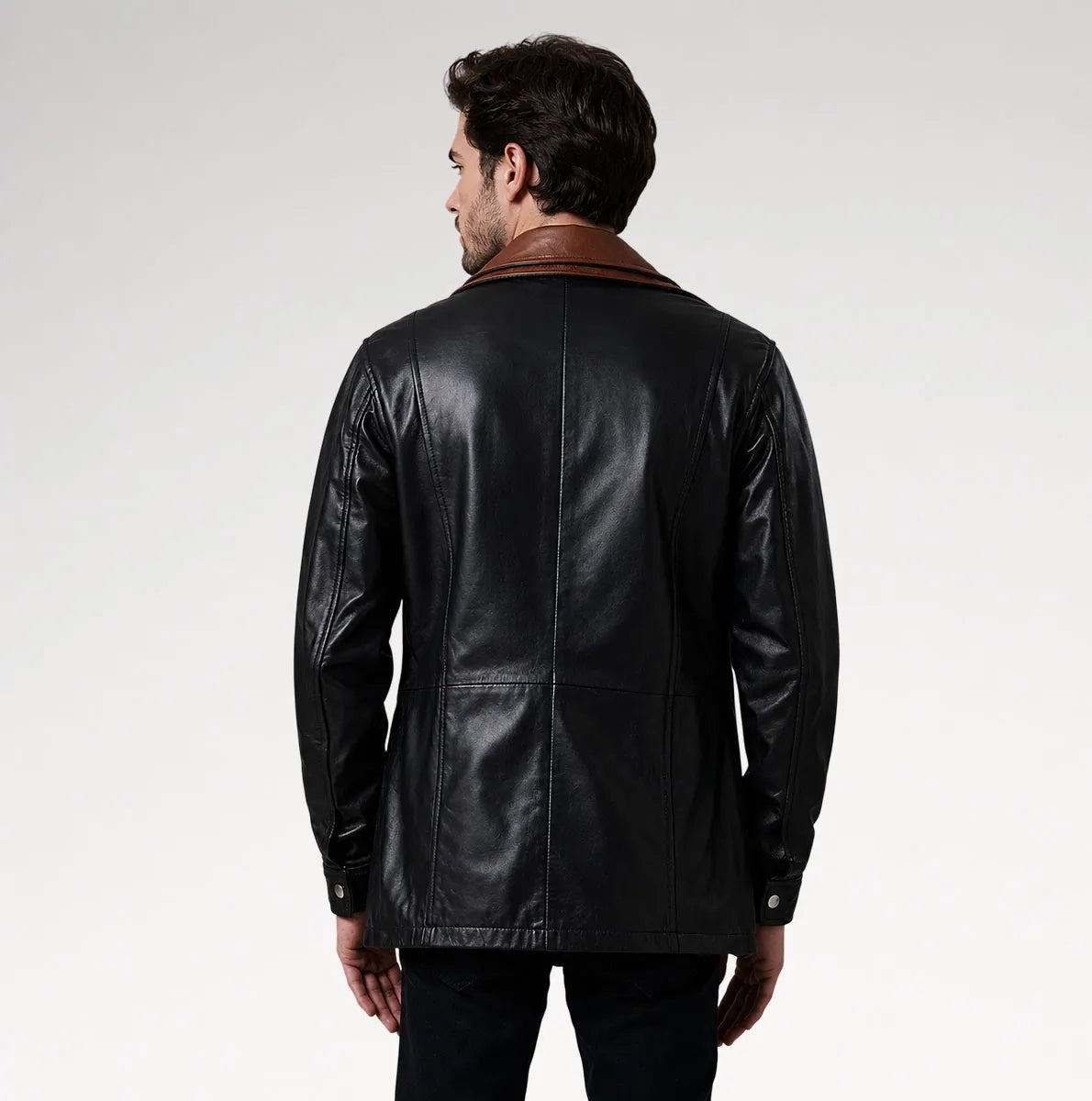 A man viewed from the back wearing a black leather jacket with a brown collar, set against a plain light gray studio background.