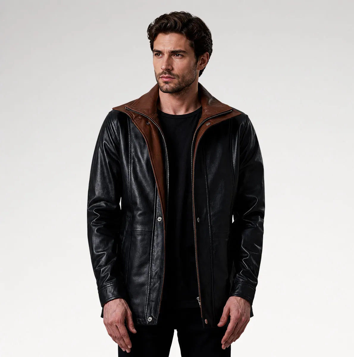 A man wearing a black leather jacket with a brown collar and lining, styled over a black t-shirt and black pants, photographed against a light gray studio background.