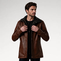 A man wearing a brown leather jacket with a black collar and zipper, styled over a black shirt, photographed against a light gray studio background.