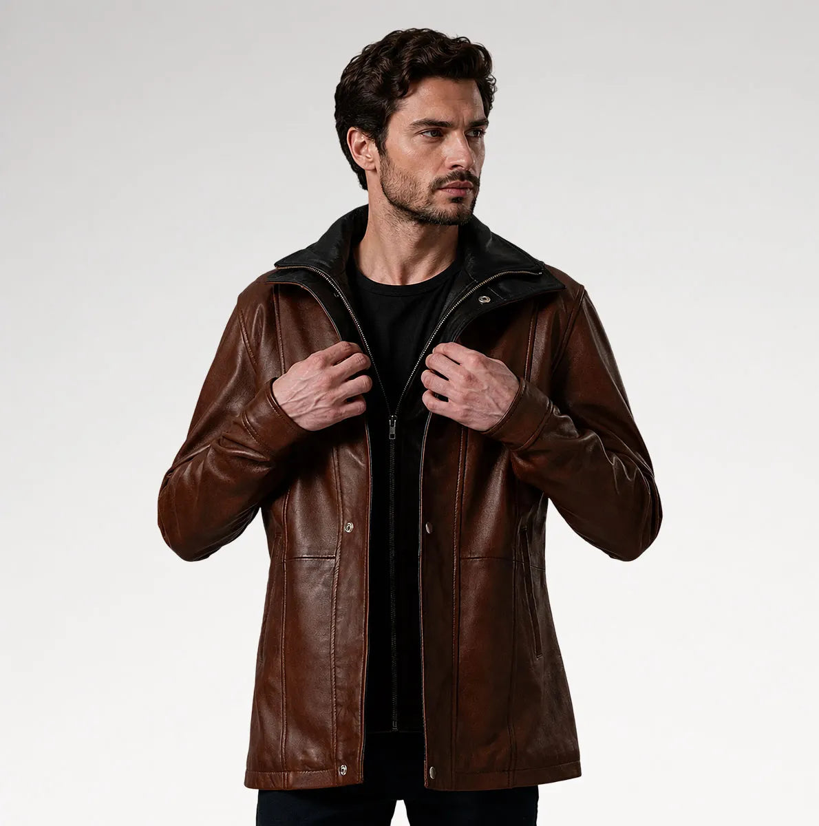 A man wearing a brown leather jacket with a black collar and zipper, styled over a black shirt, photographed against a light gray studio background.