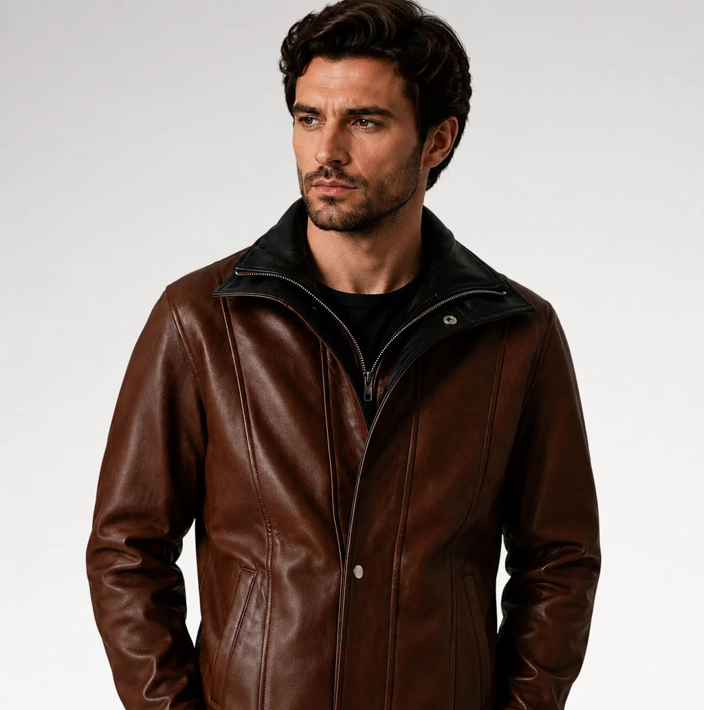 A man wearing a brown leather jacket with a black collar and zipper, photographed against a light gray studio background.
