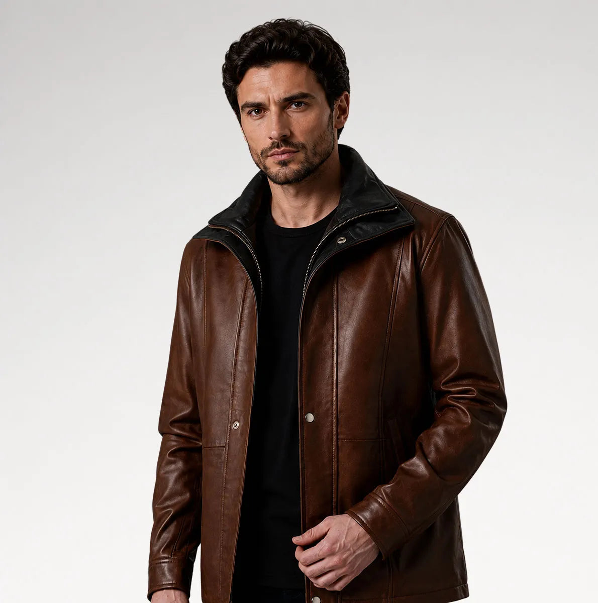 A man wearing a brown leather jacket with a black inner collar and a black t-shirt, photographed against a light gray studio background.