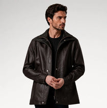 A man wearing a dark brown leather jacket over a black shirt, photographed against a light gray studio background.