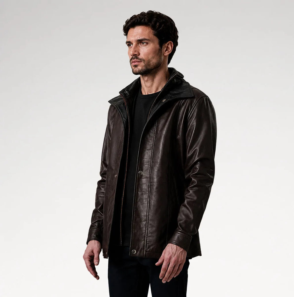 A man wearing a dark brown leather jacket with a high collar over a black shirt, photographed against a light gray studio background.