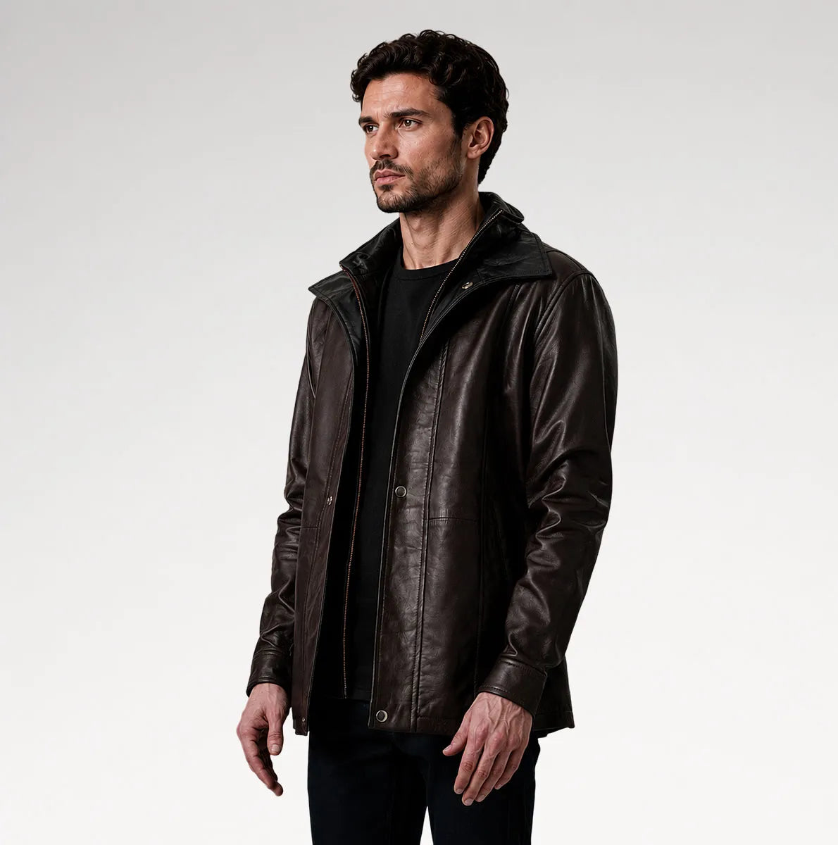 A man wearing a dark brown leather jacket with a high collar over a black shirt, photographed against a light gray studio background.