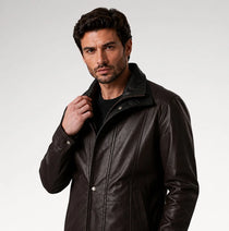A man wearing a dark brown leather jacket over a black shirt, photographed against a light gray studio background.
