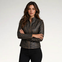 A woman modeling a dark brown distressed leather jacket with quilted shoulder panels and a front zipper, paired with black pants, against a light gray studio background.