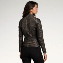 A woman shown from the back wearing a dark brown distressed leather jacket with quilted shoulder panels and zippered sleeves, paired with black pants, against a light gray studio background.