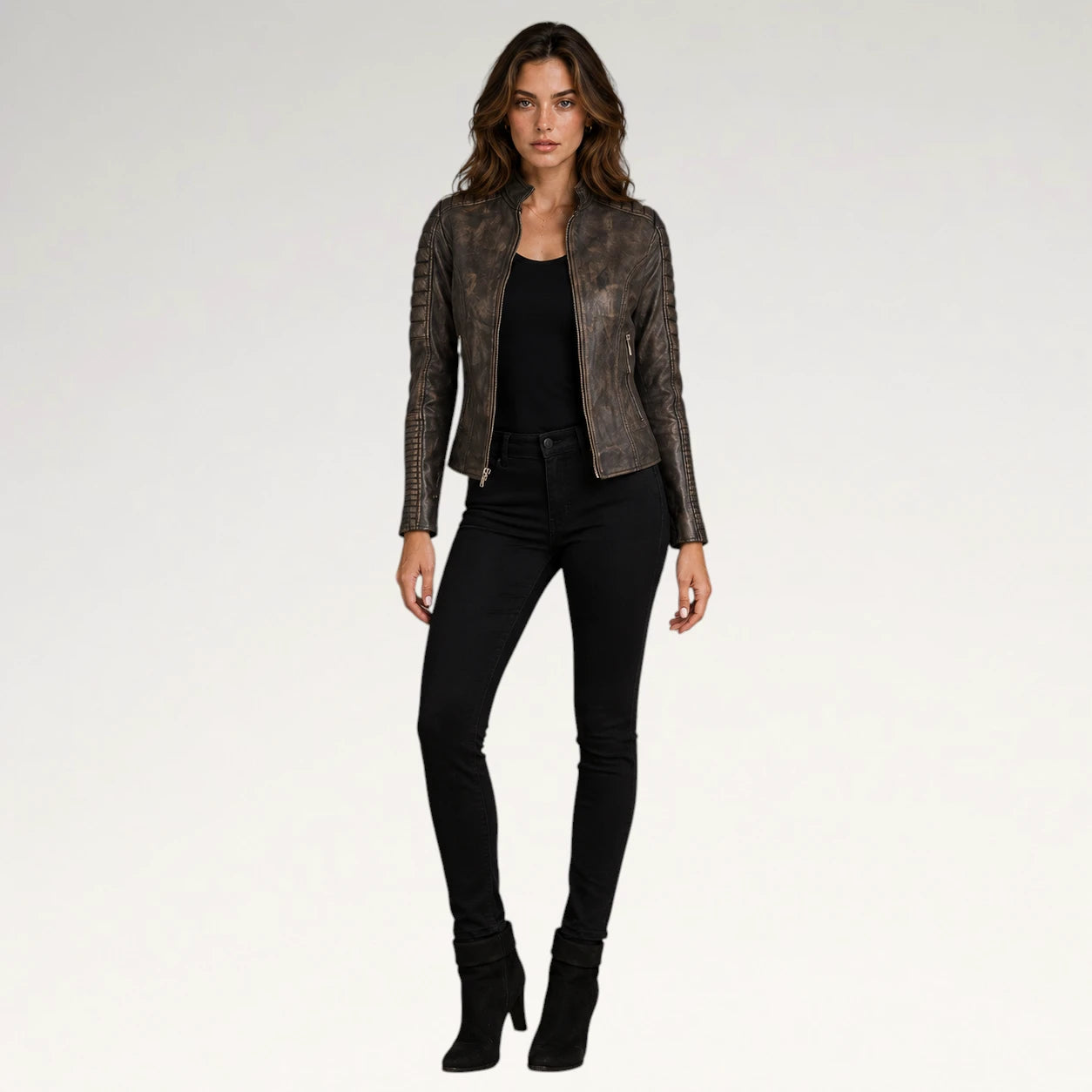A woman modeling a dark brown textured leather jacket with a snakeskin pattern, worn over a black top and black skinny jeans, against a light gray studio background.