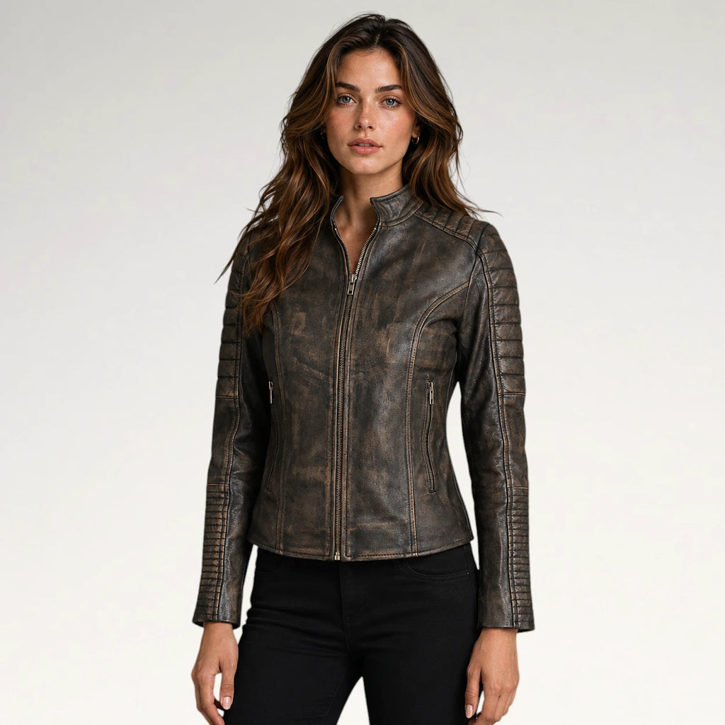 A woman modeling a distressed brown faux leather moto jacket with a front zipper, zip pockets, and ribbed sleeve details, paired with black pants against a light gray studio background.