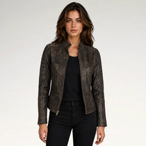 A woman modeling a distressed dark brown faux leather moto jacket with silver zippers, worn over a black top and black jeans, against a plain light gray background.