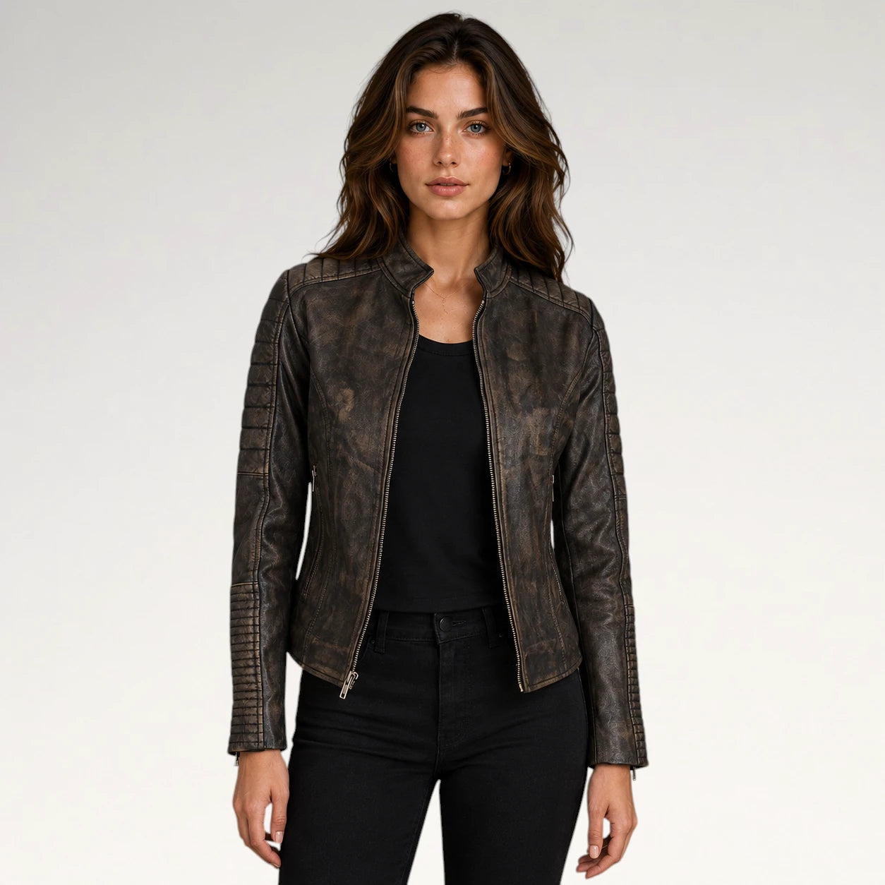 A woman modeling a distressed dark brown faux leather moto jacket with silver zippers, worn over a black top and black jeans, against a plain light gray background.